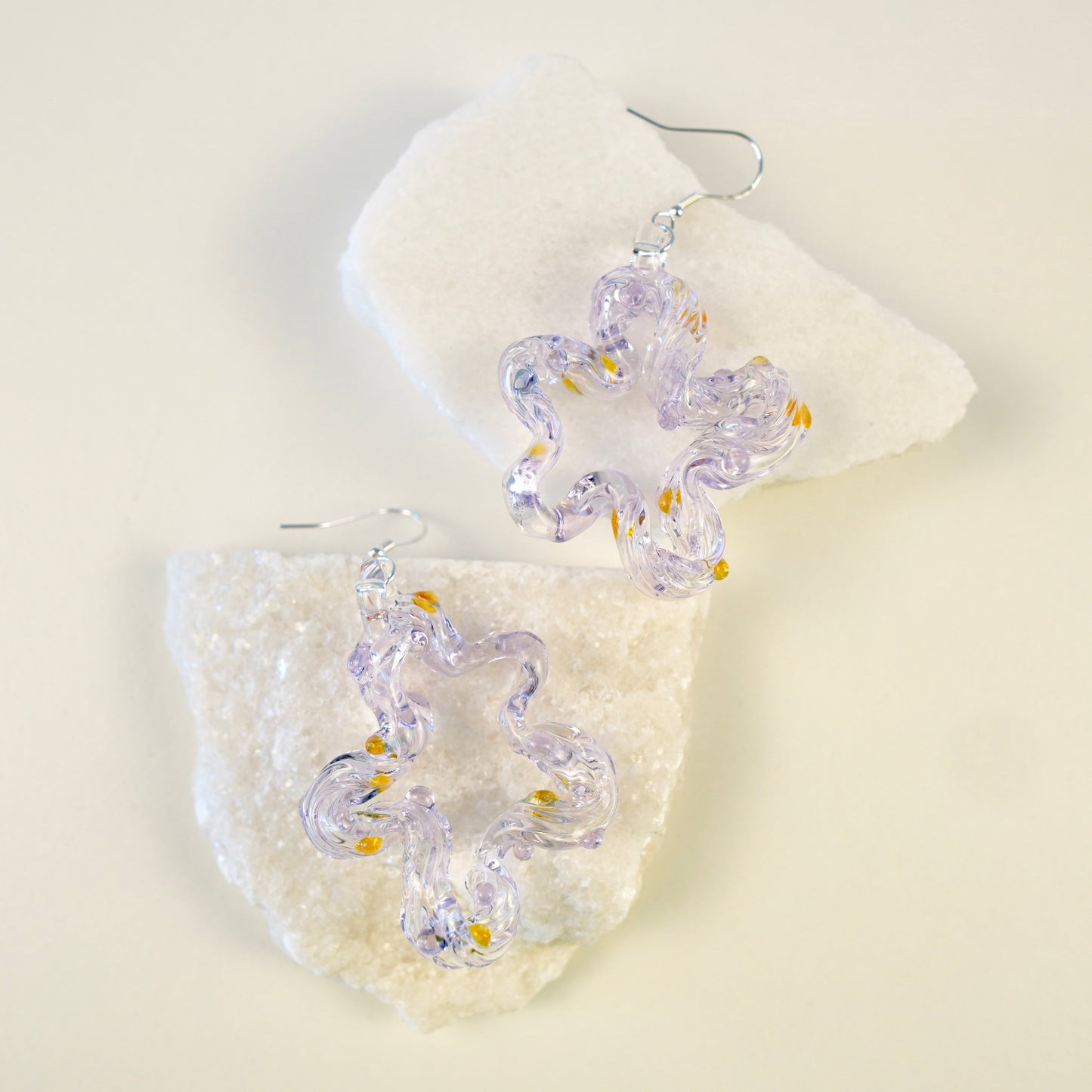 Clear glass earrings with yellow accents on a white stone background